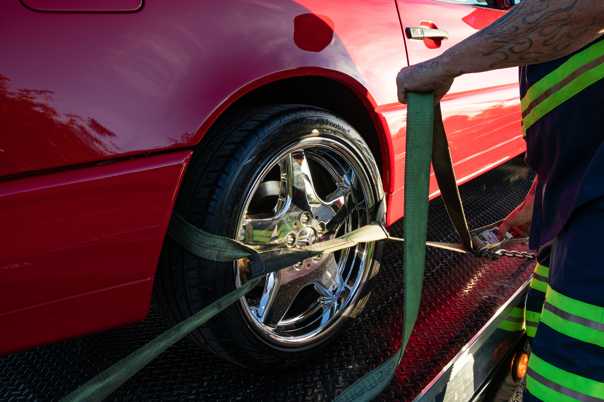 Crown tow operator securing a red vehicle to the flatbed with wheel straps