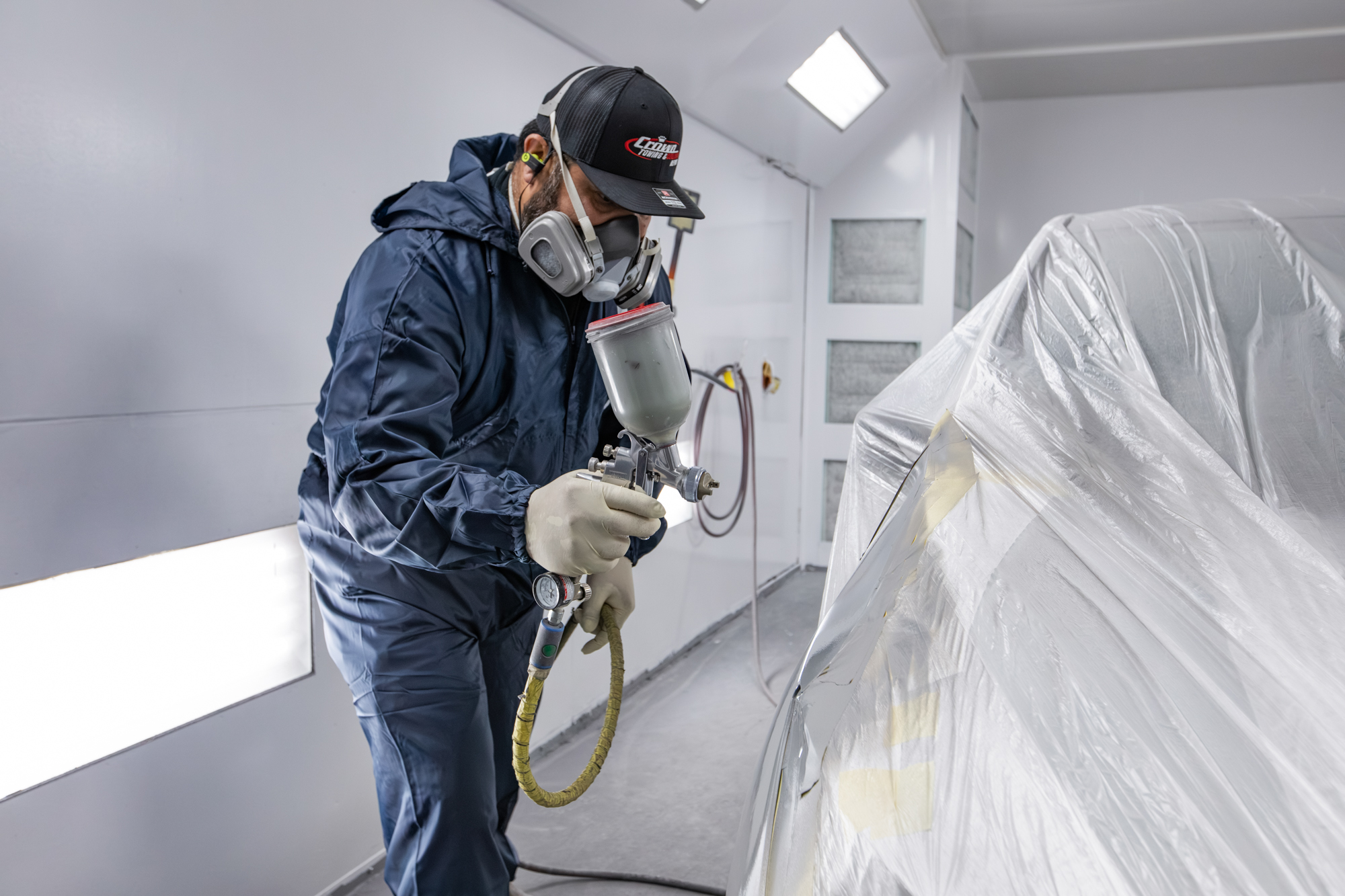 Crown painter spraying base coat inside the downdraft paint booth