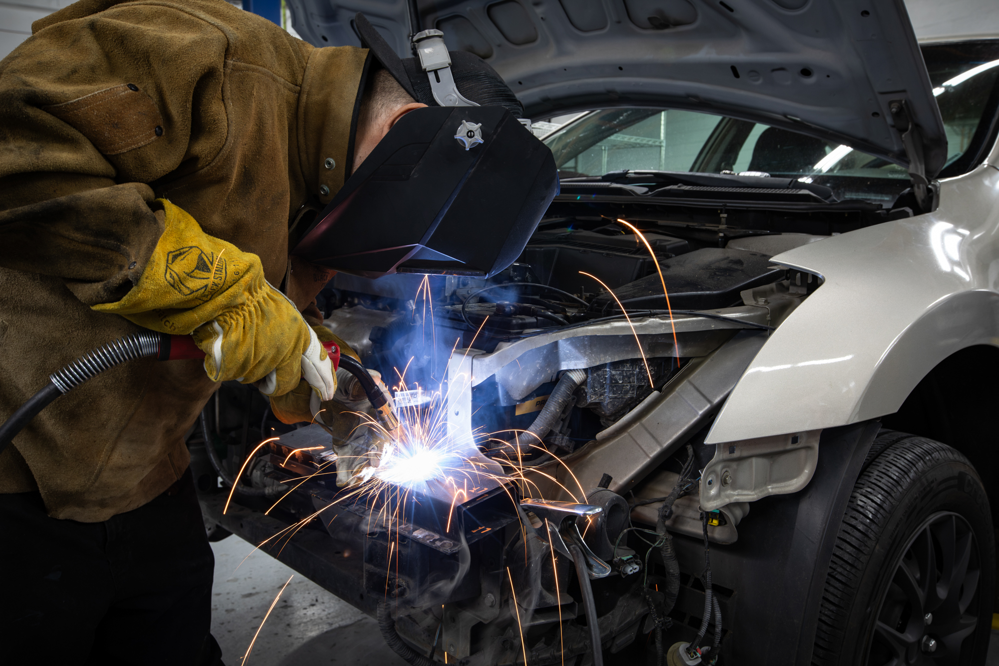 Crown I-CAR Gold Class technician MIG welding a vehicle frame during collision repair